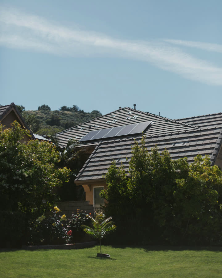 A home with a tile roof and solar panels, surrounded by garden, with hills behind