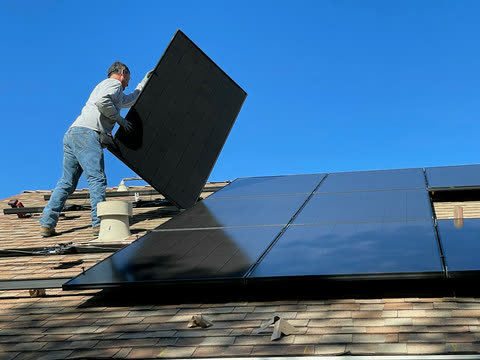 An installer lifts a solar panel onto a home’s roof