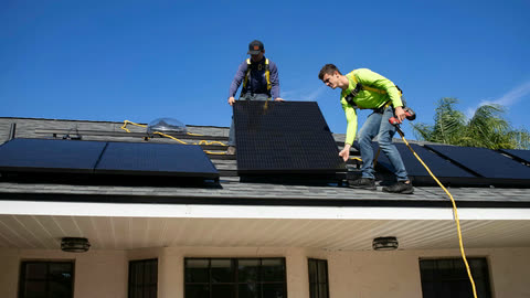 Dos instaladores colocan paneles solares en el techo de una casa