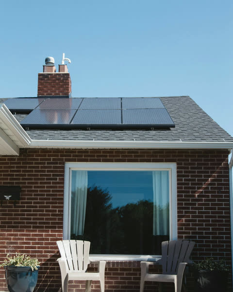 A home with solar panels above the porch, two chairs in front of the window